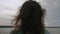 Defocused back view of brunette with long hair dancing on pier in front of water. Sky and water on background are in