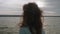 Defocused back view of brunette with long hair standing on pier in front of water. Sky and water on background are in