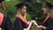 Defocused female graduates in academic dress talking, holding diplomas in hands