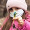 Defocused girl in a protective mask with a spring flower in her hand. Little european girl wearing mask for protect pm2.5 and