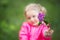 Defocused portrait of little 3 years old blonde girl in pink jacket with branch of purple lilac in hand. Blossom spring concept.