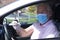 Defocused senior man with facial mask and protective gloves due to coronavirus ready to drive his car - new normal life until the