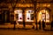 Defocused view of the city street with windows framed with Christmas lights. Night time. Pedestrians walking on the