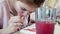 Defocused view of glass of water on foreground and focused view of blond girl colouring details of picture in mint