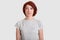 Dejected miserable woman with red hair, minimal make up, looks in displeasure at camera, wears casual grey t shirt, expresses