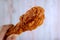 Delectable Crispy Fried Chicken Drumstick in Hand against Blurry Grunge Wooden Wall