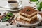 A delectable piece of tiramisu cake rests elegantly on a plate next to a steaming cup of coffee, creating a perfect