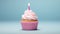 Delectable single birthday cupcake with a lit candle on a charming light pink background