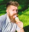 Delicacy concept. Man with long beard eats ice cream, while sits on grass. Bearded man with ice cream cone. Man with