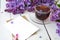 Delicate morning tea table setting with lilac flowers, a transparent cup of tea and a saucer and a white vase, white and