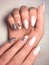 Delicate pink gel polish on long nails with a silver design. Nude manicure with a brilliant design.