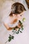 Delicate rose in the hands of fascinating young girl dressed white wedding gown