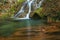 Delicate waterfall in the forest and autumn foliage