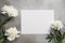 Delicate white peonies with a blank white paper on a gray concrete background.