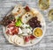 Delicious appetizer to wine - ham, cheese, grapes, crackers, figs, nuts, jam, served on a light wooden board, and two glasses with