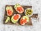 Delicious appetizers - cream cheese, smoked salmon and avocado sandwiches and olives on a wooden board. On a light background
