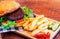 A delicious beef burger with fries served on a wooden board, a tasty burger with vegetables, ketchup, and french fries on a wooden