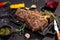 Delicious beef steak on black stone cutting board. Grilled meat served with knif, grilled corn, garlic, rosemary, sauces, chilli