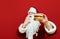 Delicious big burger holds Santa Claus in his hand and wants to eat. Portrait of hungry Santa isolated on red background with