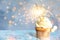 Delicious birthday cupcake with sparkler on blue table against blurred lights. Space for text