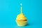 Delicious birthday cupcake with yellow cream and candle on light blue background