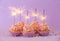 Delicious birthday cupcakes with firework candles on color background