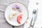 Delicious bite of colorful donuts with sprinkles on stylish plate on white table with confetti, fork and knife, flat lay. Party