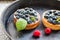 Delicious blueberry tartalets with vanilla cream and fresh raspberry berries on a black cast iron plate.