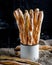 Delicious breadsticks grissini. Italian appetizers. Wooden dark background and burlap in metal oldstyle cup.