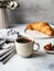 Delicious breakfast - the cup of coffee, croissant, berries and various magazins on the table at the grey background. Copy space