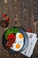 Delicious breakfast with fried eggs, crispy bacon, cherry tomatoes and arugula served on the wooden table with knife and fork