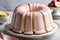 A delicious bundt cake with pink and white icing on a white plate, with strawberries. marble background