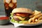 Delicious burger, soda drink and french fries served on grey table, closeup