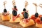 Delicious canape with melon, prosciutto and olives on wooden board against white background