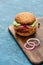 Delicious cheeseburger on wooden board on blue textured surface