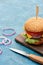 Delicious cheeseburger on wooden board near knife on blue textured surface