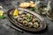 Delicious cooked sea escargo snails with herbs, butter, garlic on metal plate with forks. wine glass. gourmet food. Restaurant