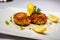 Delicious crab cakes with crispy golden crust served on a white plate with lemon wedges and green herbs garnish