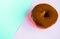 Delicious donut with shiny chocolate icing on pastel pink-blue background, close-up, Top view