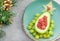 Delicious edible Christmas tree of avocado, frozen sweet raspberries and grapes on a blue plate on the table near the branches of
