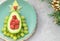 Delicious edible Christmas tree of avocado, frozen sweet raspberries and grapes on a blue plate on the table near the branches of