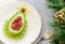 Delicious edible Christmas tree of avocado, frozen sweet raspberries and grapes on a blue plate on the table near the branches of