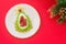 Delicious edible Christmas tree of avocado, frozen sweet raspberries and grapes on a white plate on a red table near the branches