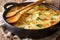 Delicious Finnish baked potatoes with anchovy fillets, onions and heavy cream close-up in a frying pan