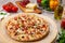 Delicious fresh baked supreme vegetable and meat pizza on wooden board with italian food ingredients, vertical