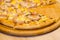 Delicious fresh pizza with ham, mushrooms, corn on wooden tray and table in cafe, piece of pizza has already been eaten