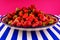 Delicious fresh strawberries on a huge earthenware dish on a blue-and-white striped table.