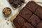 Delicious freshly baked brownies, walnuts and pieces of chocolate on white wooden table, flat lay