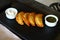 Delicious fried cheburek pies on the dark plate with two sauces