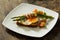 Delicious fried egg on a toasted bread, covered with grilled asparagus wrapped in bacon on a white plate.